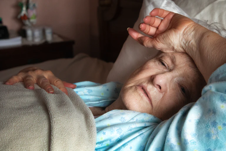 An older woman lays in bed, sick with COVID