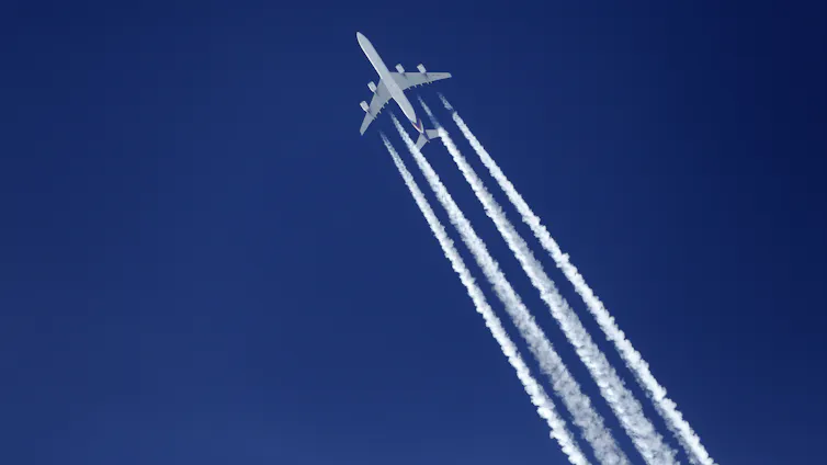 A plane flying through the sky, leaving behind a trail of vapour.