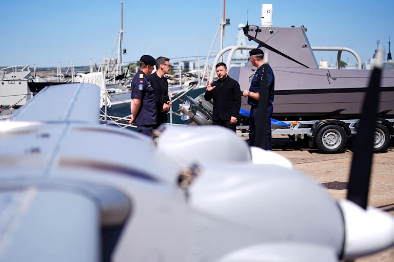 UK prime minister, Andy Burnham, and Ukrainian president, Volodymyr Zelensky, with Ukrainian military personnel at a UK naval base inspecting a drone.