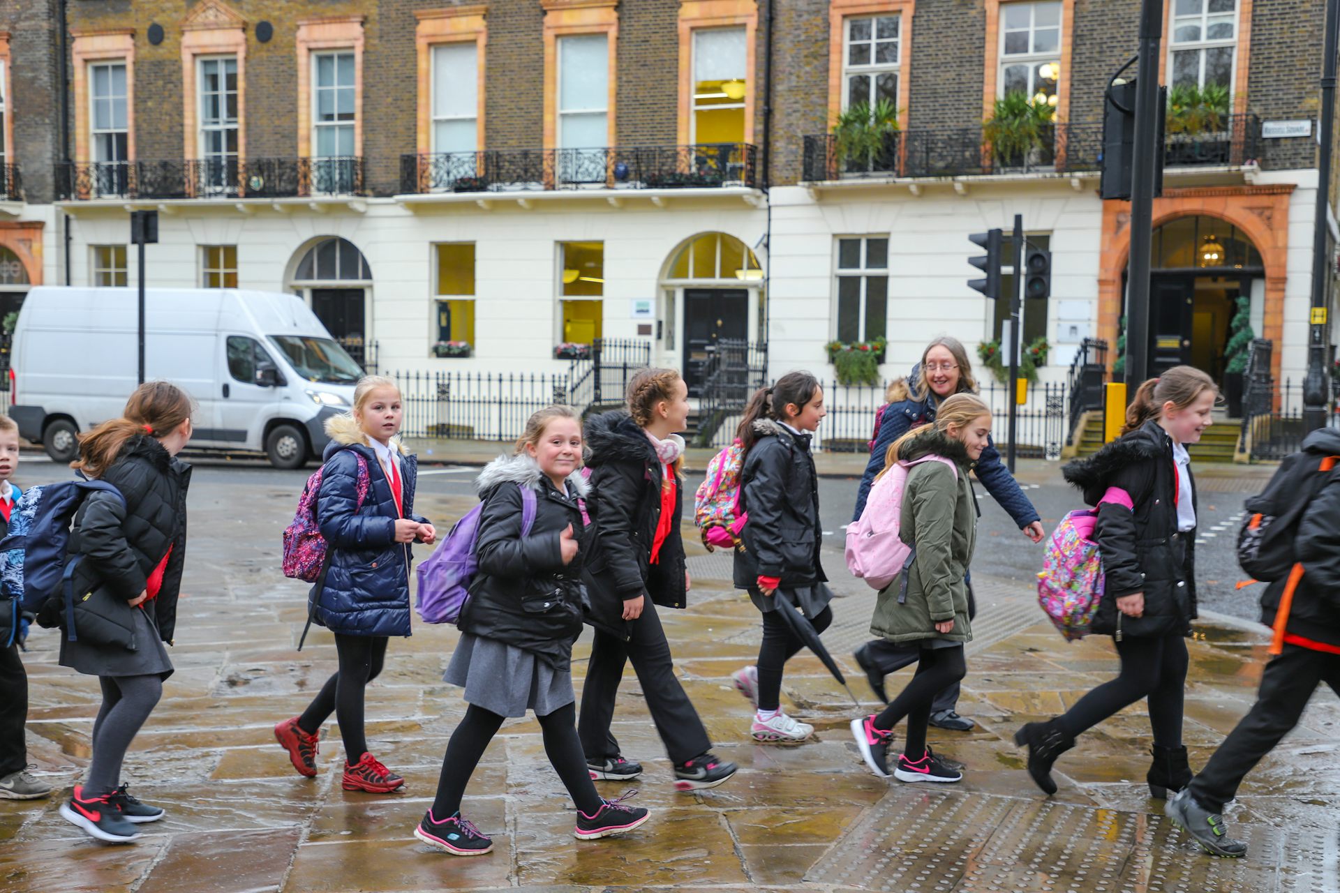 A group of schoolchildren wearing uniforms and winter coats walk along a road in Westminster with their teachers.