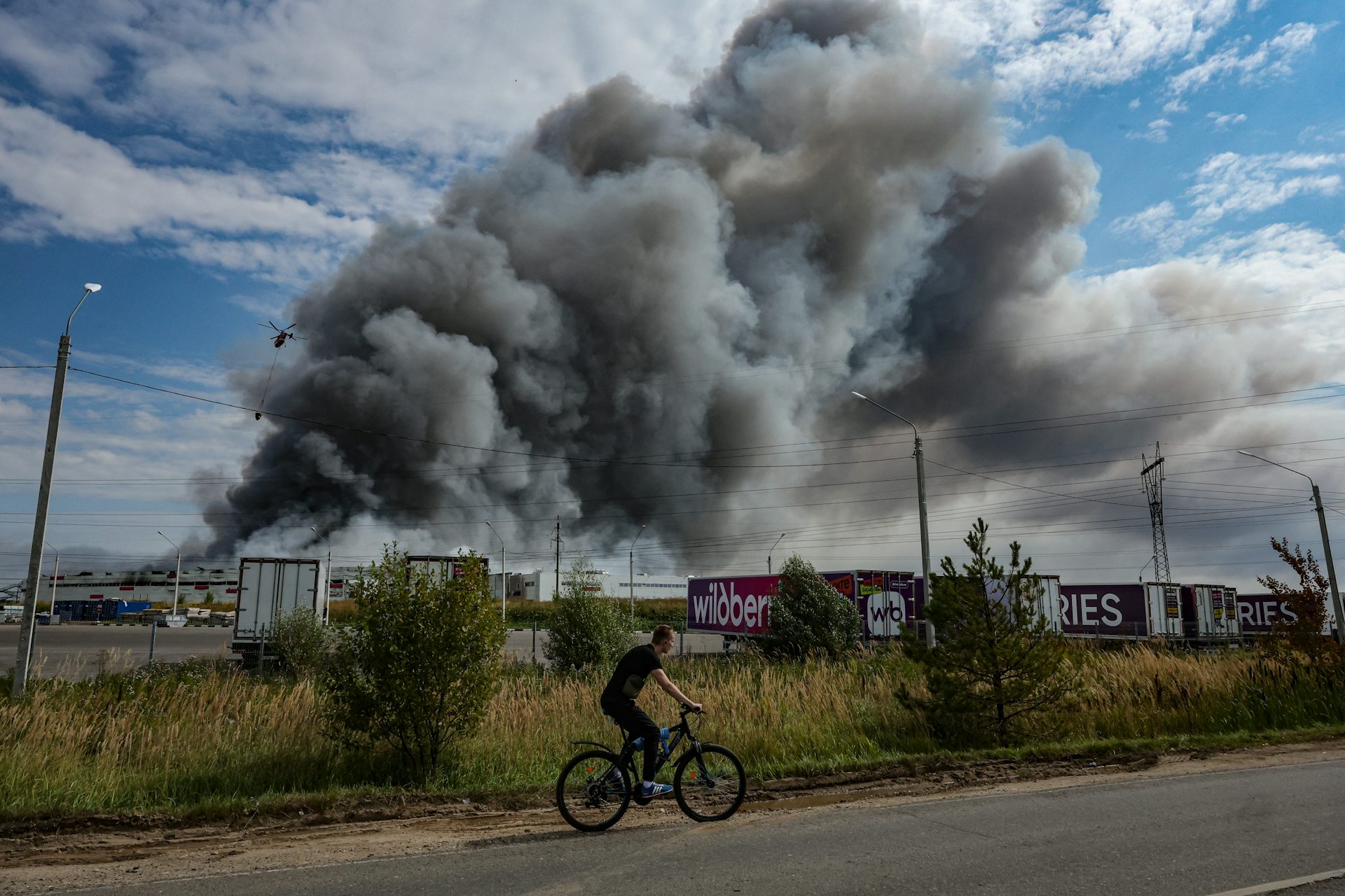 A man cycles past a warehouse on fire after a drone strikes, Podolsk, Moscow Region, August 16 2026.
