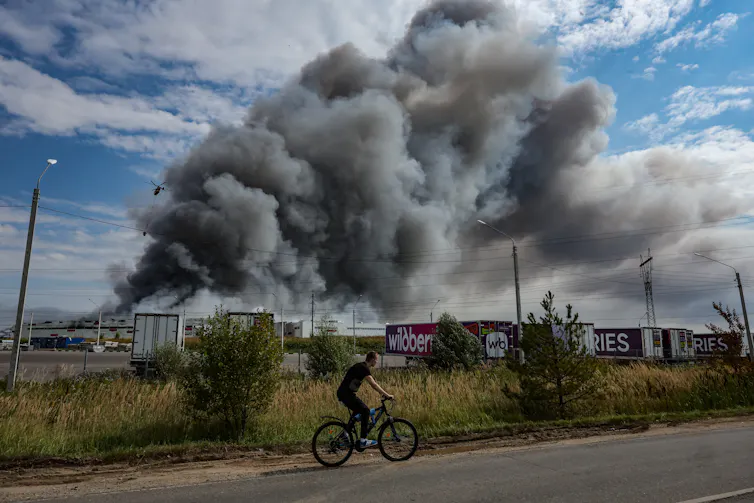 A man cycles past a warehouse on fire after a drone strikes, Podolsk, Moscow Region, August 16 2026.