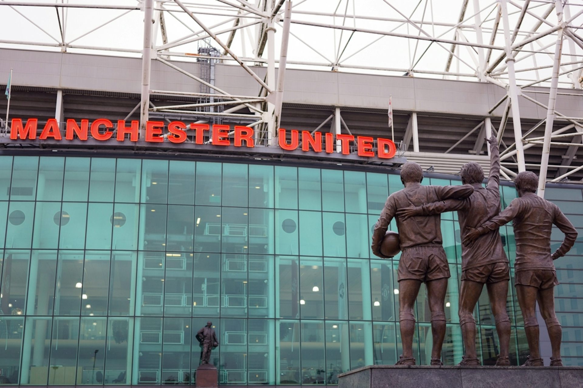 Old Trafford stadium with statues of three famous players outside