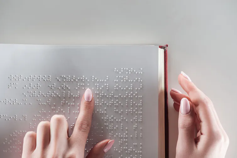 Top view of young woman reading braille text on white pape.