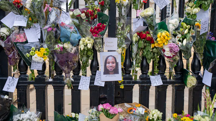 A photo of a young Black man with dreadlocks affixed to a black fence, surrounded by colorful flowers and handwritten notes.