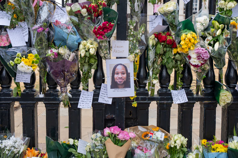 A photo of a young Black man with dreadlocks affixed to a black fence, surrounded by colorful flowers and handwritten notes.