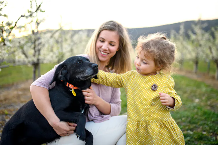 A mother with a child and both are patting the family dog.