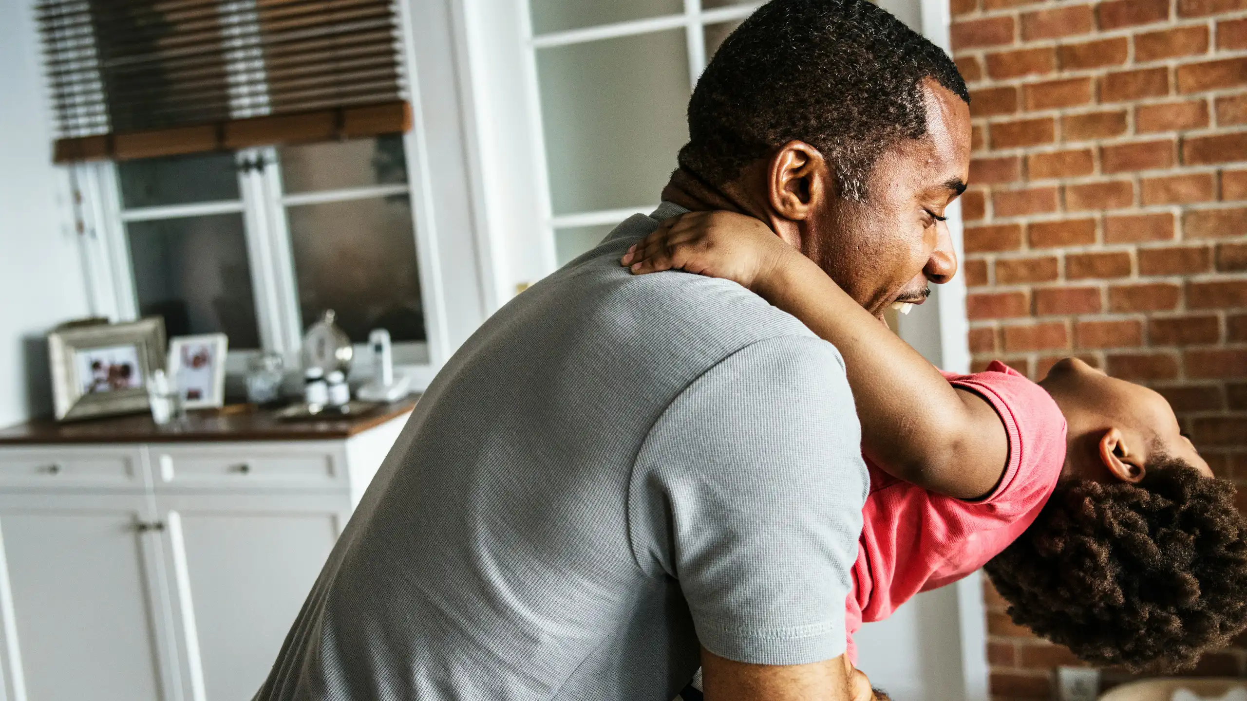 A father cradles his child who is leaning back and laughing.