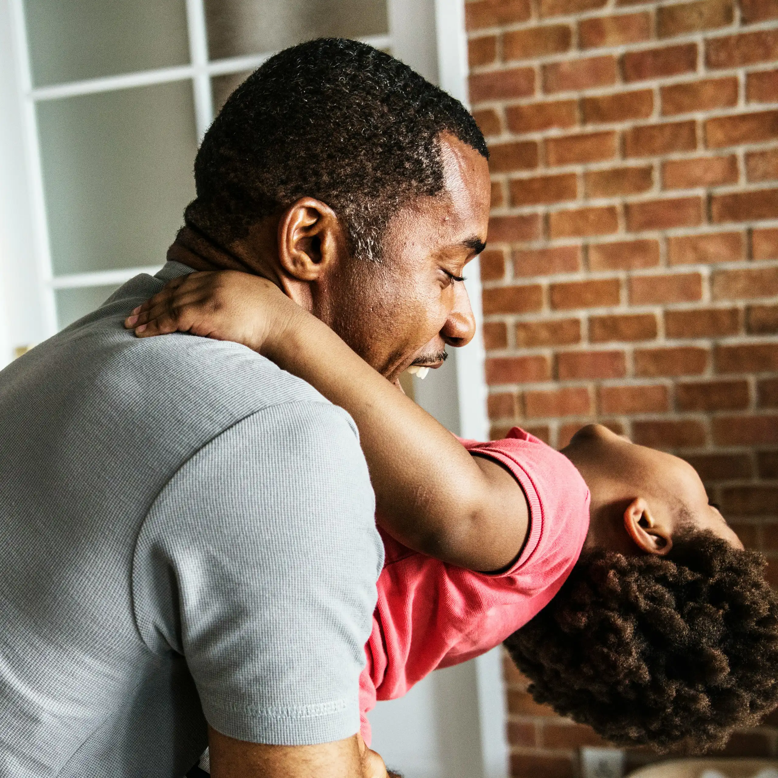 A father cradles his child who is leaning back and laughing.