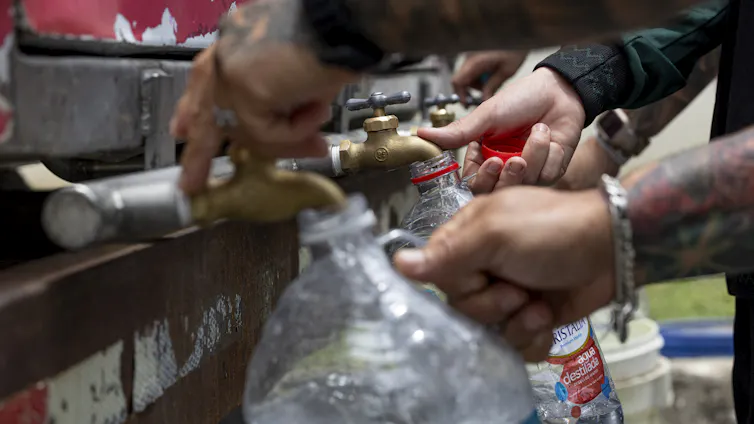 Hands holding several water jugs under spigots