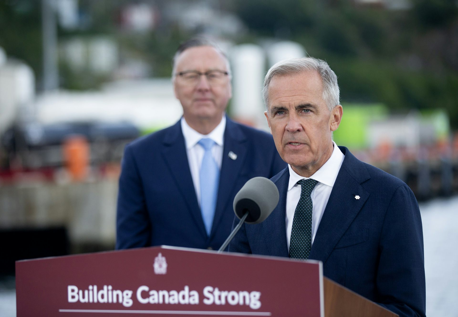 A man with short grey hair stands behind a podium that reads Building Canada Strong.