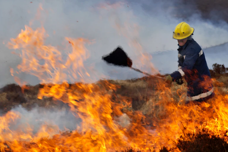 A firefighter in the middle of flames wearing protective gear.