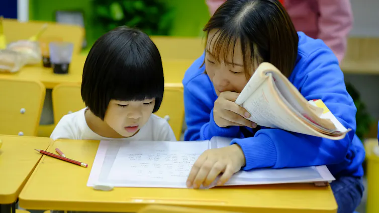 A child sits with her teacher, reading words form a sheet.