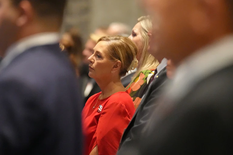 U.S. Sen. Darline Graham stands in profile in a red dress among a crowd in dark suits at a Republican Party gala.
