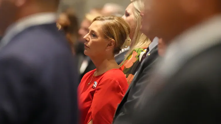 U.S. Sen. Darline Graham stands in profile in a red dress among a crowd in dark suits at a Republican Party gala.