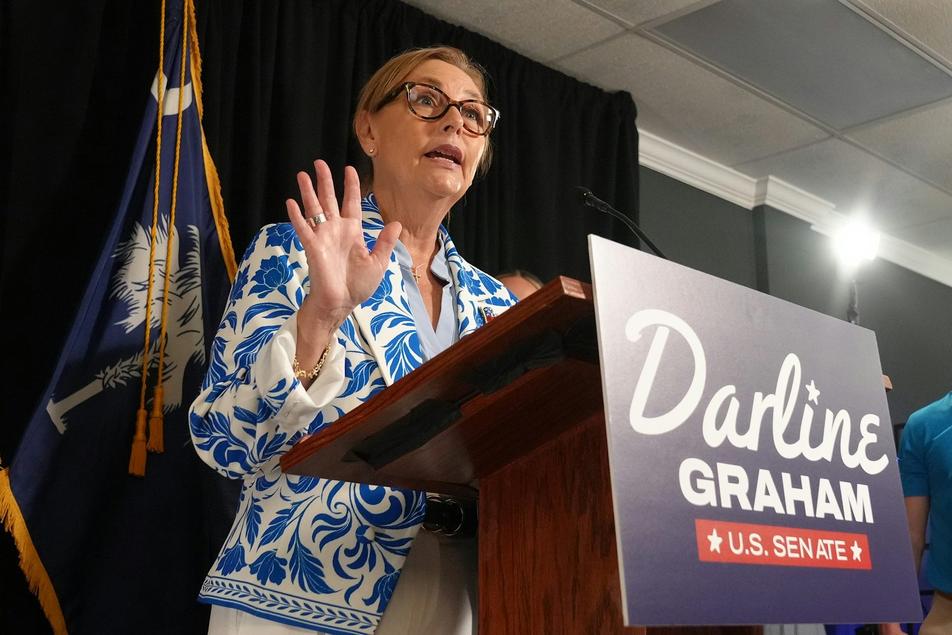 Sen. Darline Graham speaks from behind a lectern bearing a 'Darline Graham U.S. Senate' campaign sign.