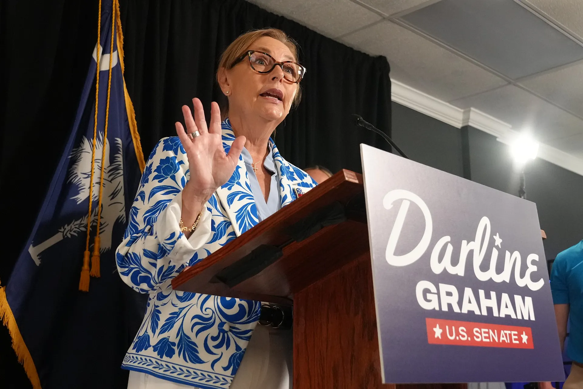 Sen. Darline Graham speaks from behind a lectern bearing a 'Darline Graham U.S. Senate' campaign sign.