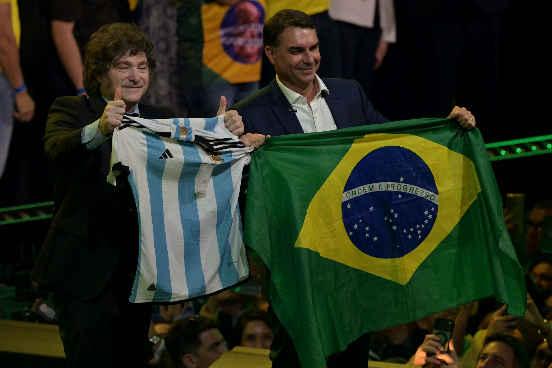 Milei et Falvio Bolsonaro sur la scène brandissent chacun le drapeau respectif de leur pays.