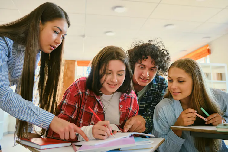 A group of students read a textbook lying open on a desk