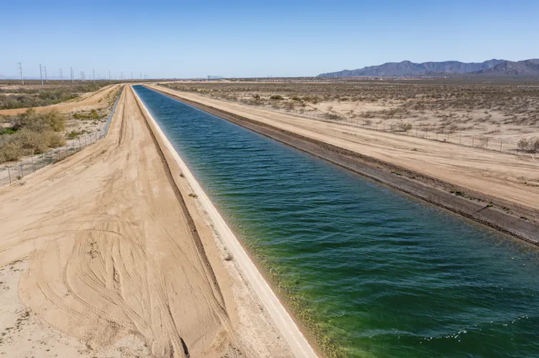 A long, straight flow of water travels through a dry desert area.