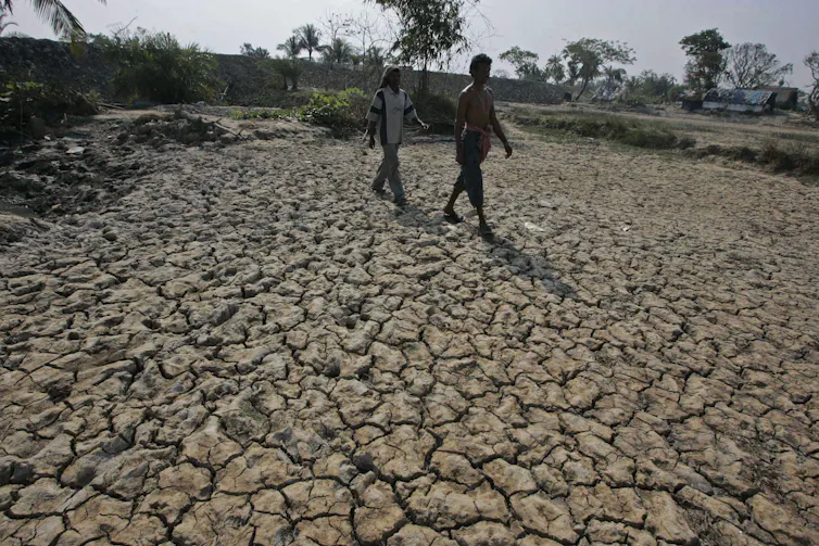 two people walk across cracked dry soil