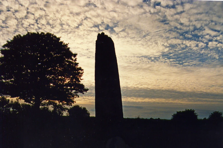 A stone monolith silhouetted against a sunset sky with gentle clouds.