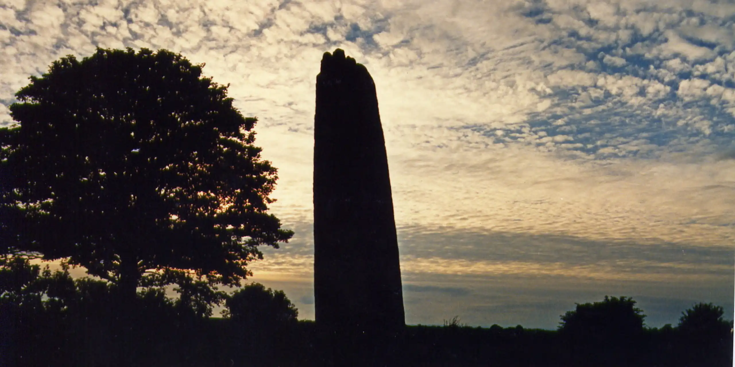 A stone monolith silhouetted against a sunset sky with gentle clouds.