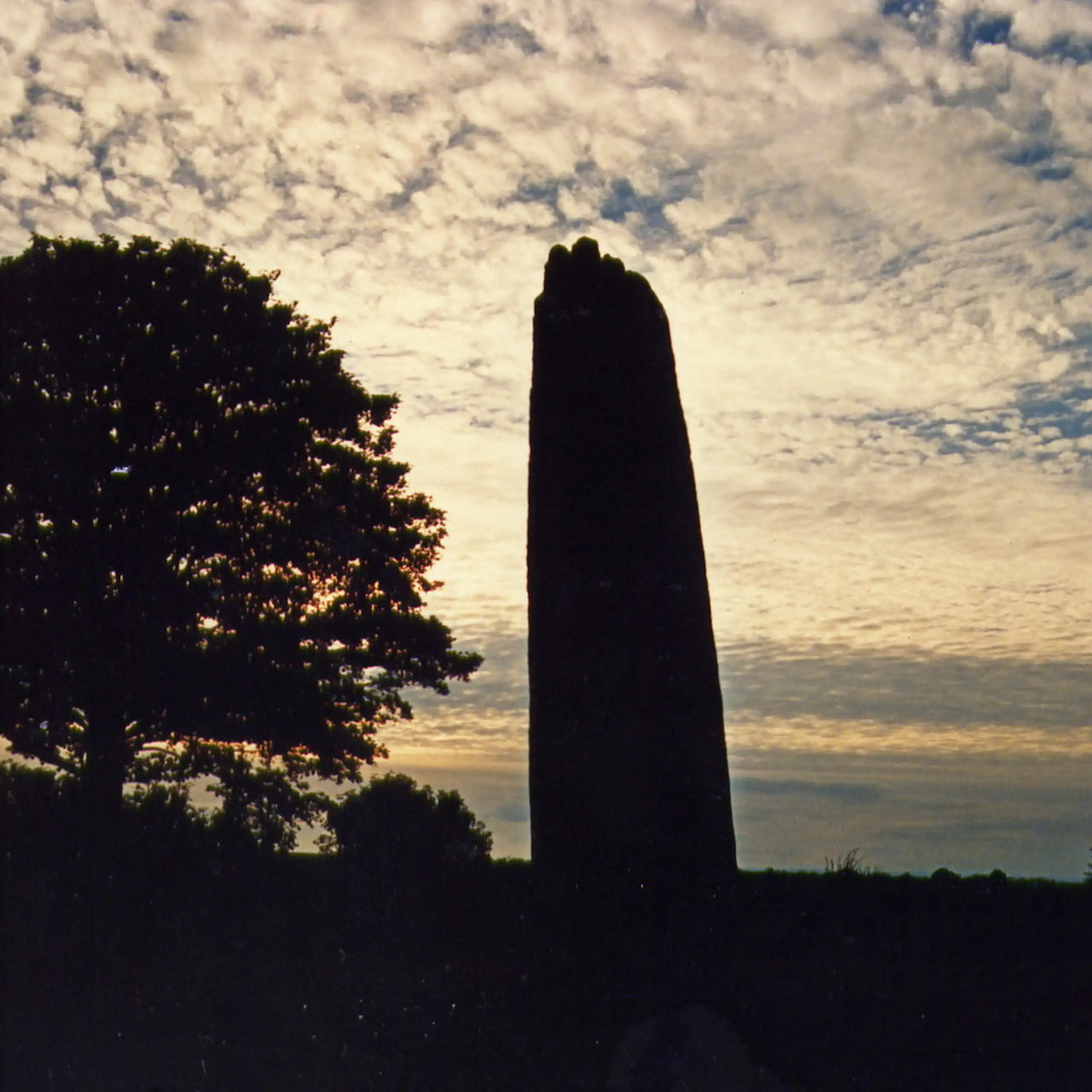 A stone monolith silhouetted against a sunset sky with gentle clouds.