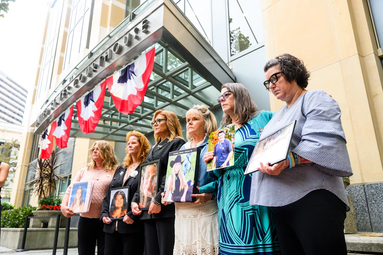 Six woman holding framed photographs outside a stone building.