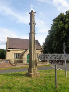 A tall, thin stone monument on a village green.