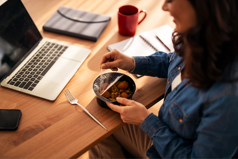 Una mujer destapa un cuenco con comida junto a un ordenador