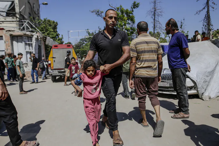 A Palestinian girl and man walk away from the site of an Israeli airstrike in Gaza City.