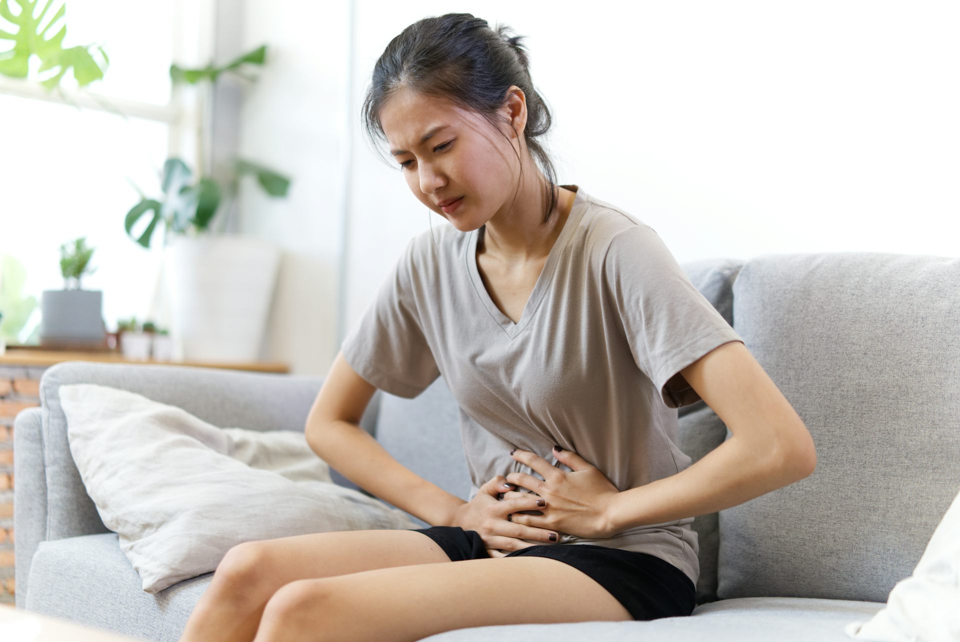Une jeune fille assise sur un canapé se tient le ventre avec ses deux mains.