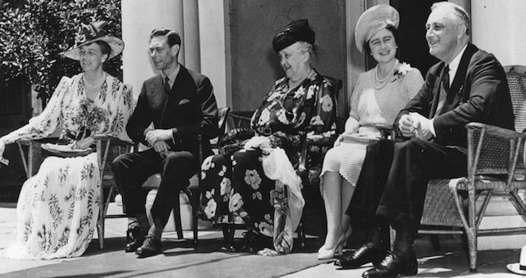 A black and white photo shows King George VI and Queen Elizabeth seated with FDR.
