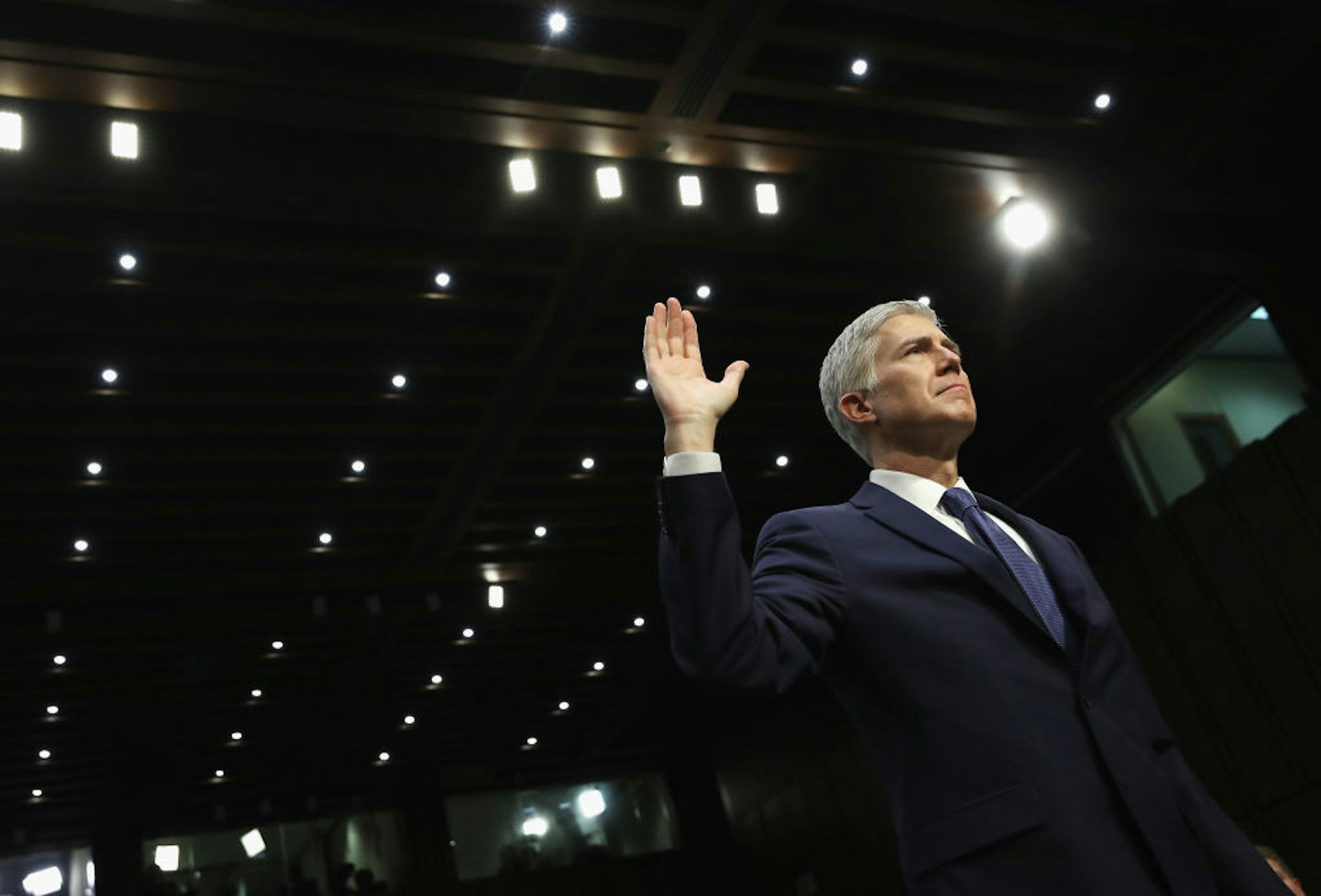 Man with gray hair wearing a suit holds his right hand in the air as he takes an oath.