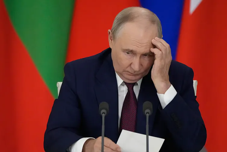 Russian president Vladimir Putin holds his hand to his head.