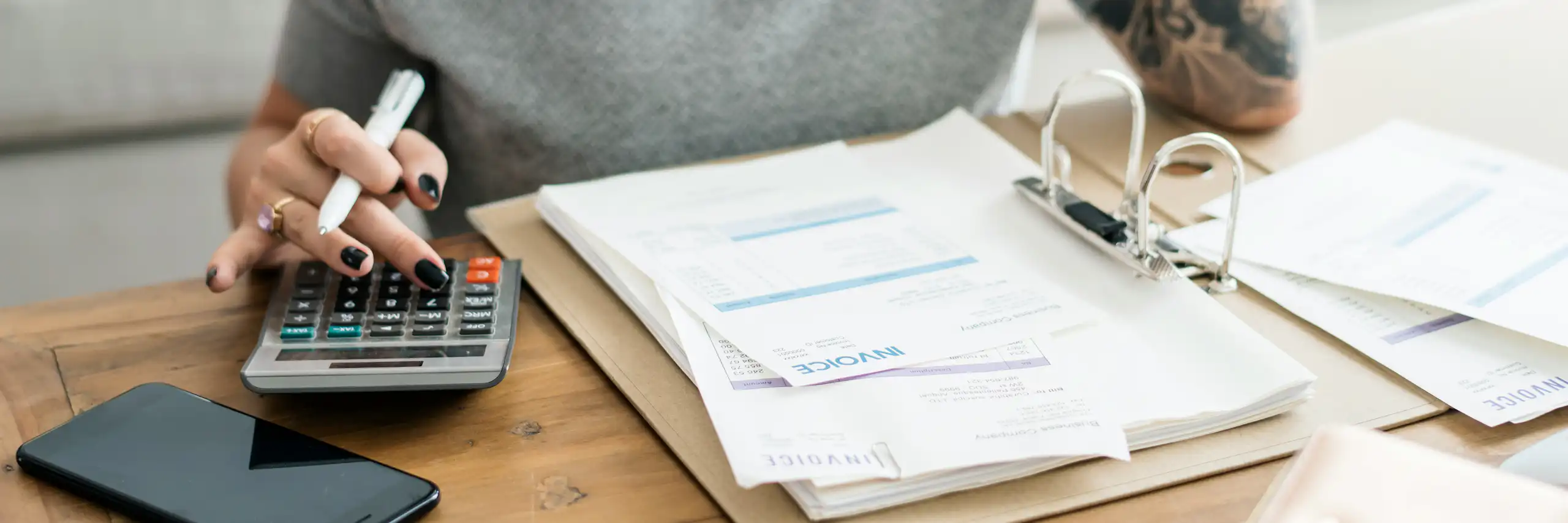 A young woman uses a calculator beside an open binder of financial documents
