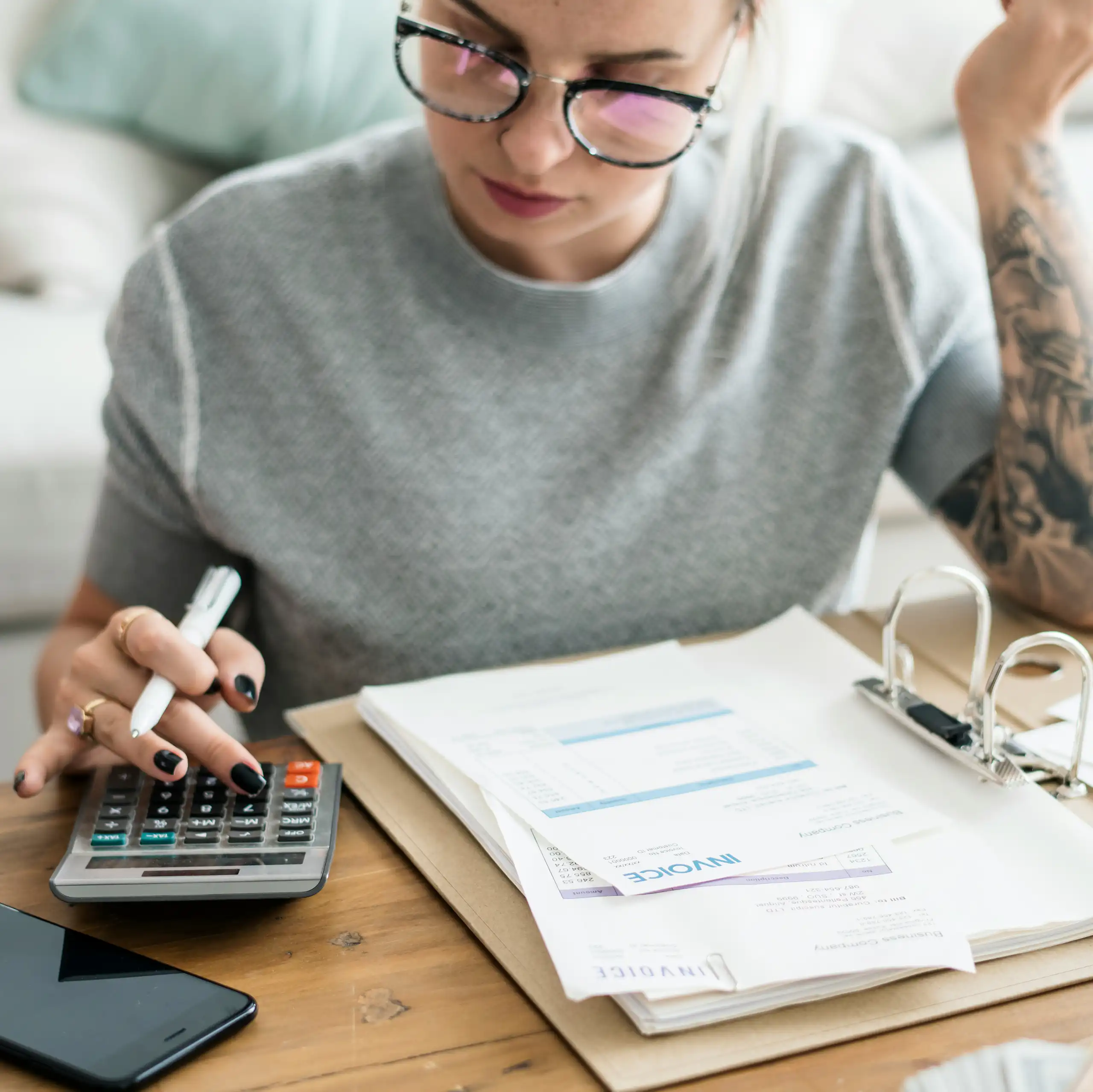 A young woman uses a calculator beside an open binder of financial documents