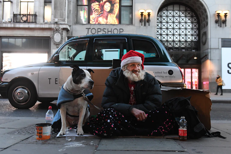 homeless man called francis sits on oxford street in london wearing a santa hat and accompanied by his dog.
