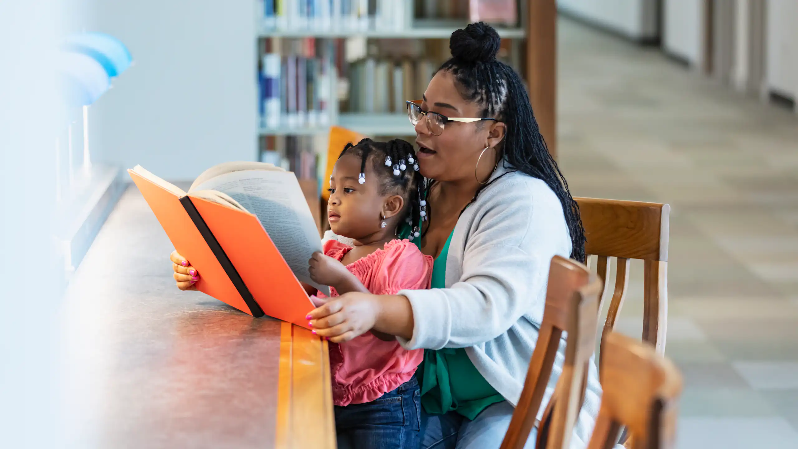 Woman sits with young girl on her lap and reads to her
