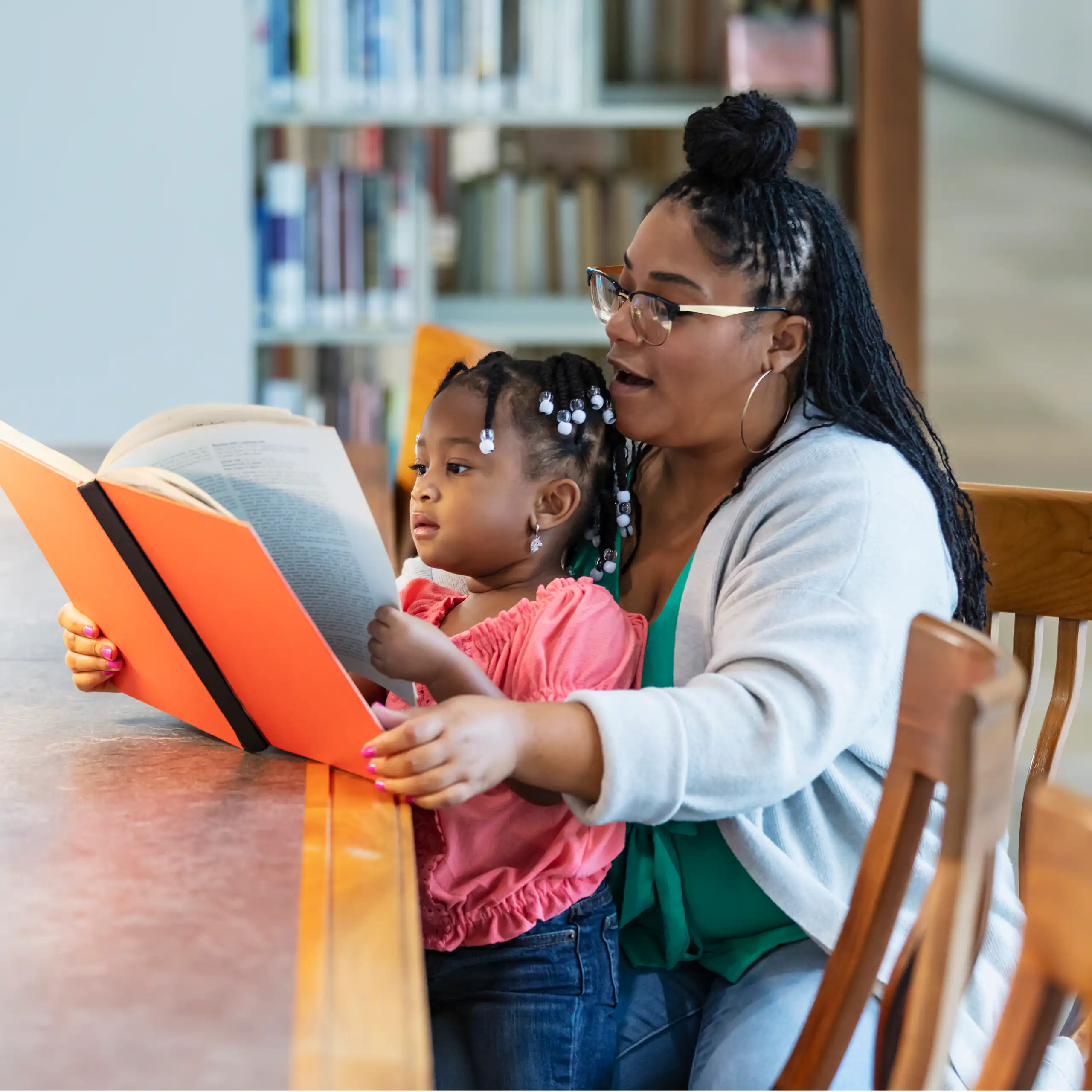 Woman sits with young girl on her lap and reads to her