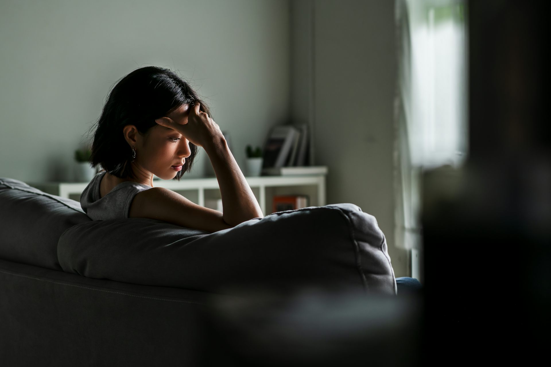  Uma jovem asiática está sentada no sofá, com um ar triste e preocupado.