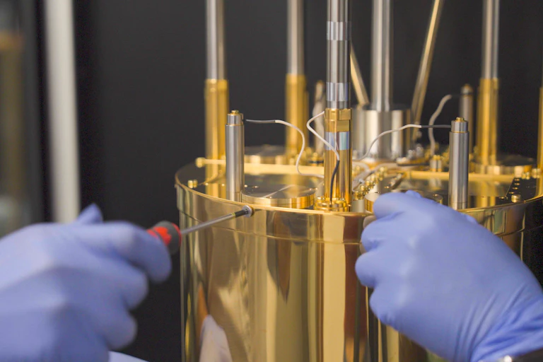 Two gloved hands touching a gold-plated cylindrical device.