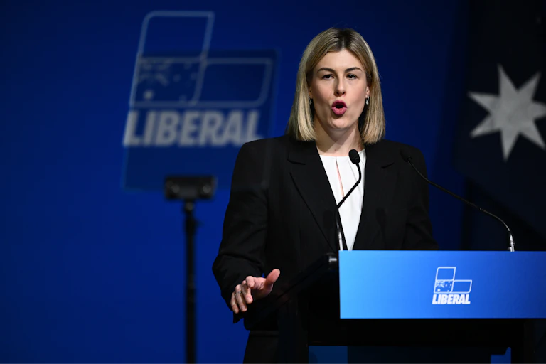 A woman with a blonde bob speaks at a lectern