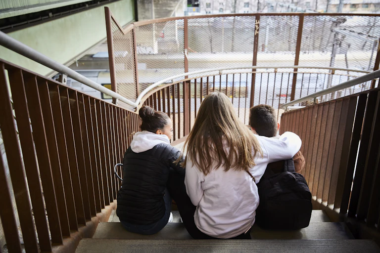 Three teens sitting on a stairwell, seen from behind.