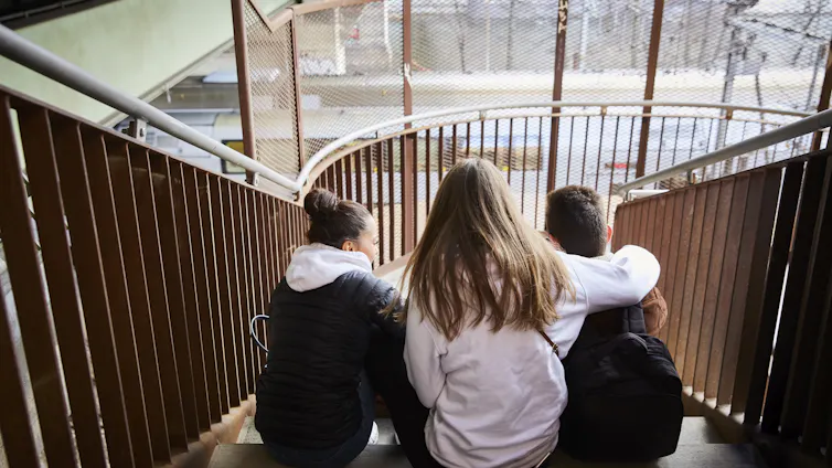 Three teens sitting on a stairwell, seen from behind.