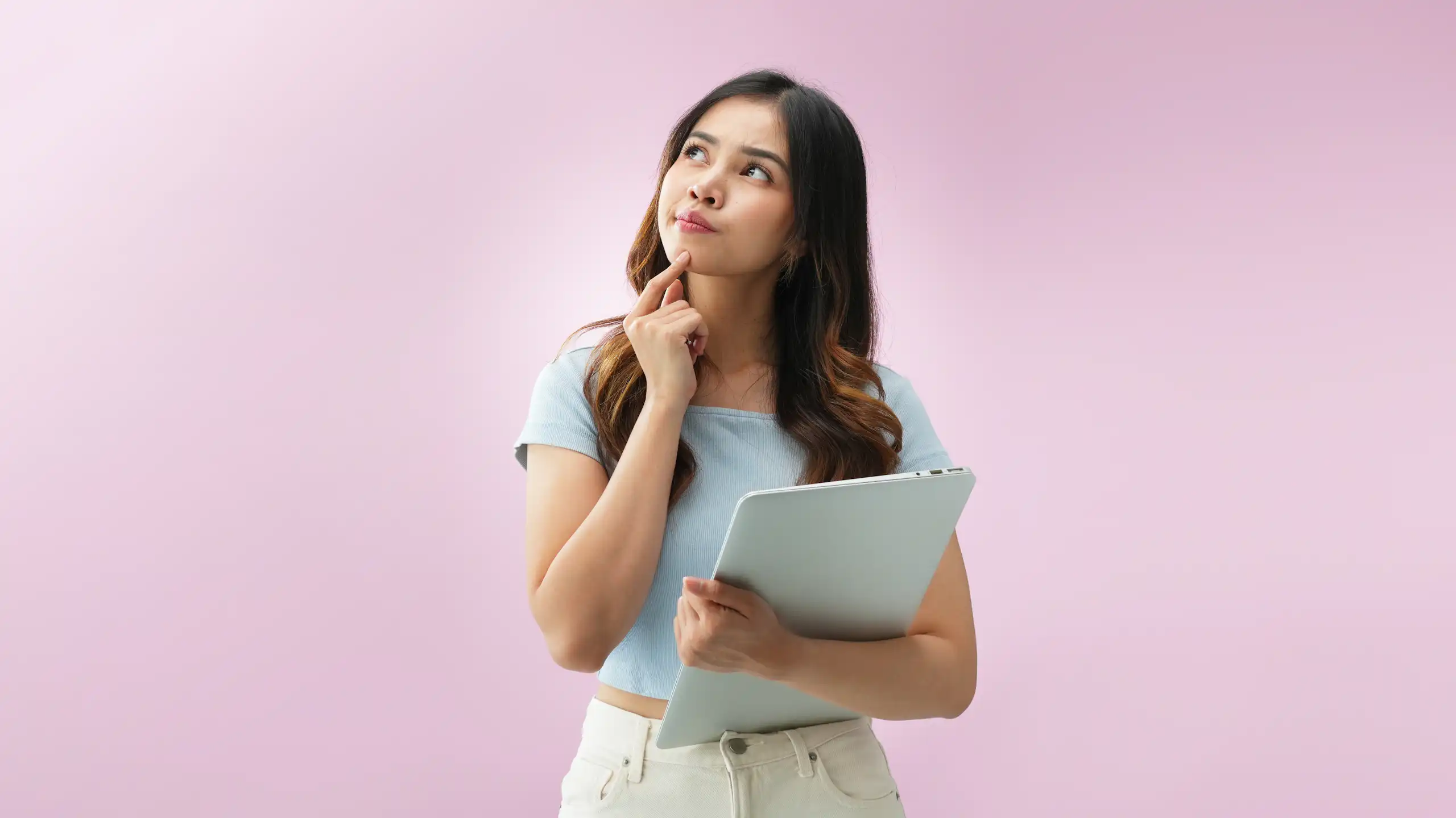 woman standing with laptop, looks questioning, pink background