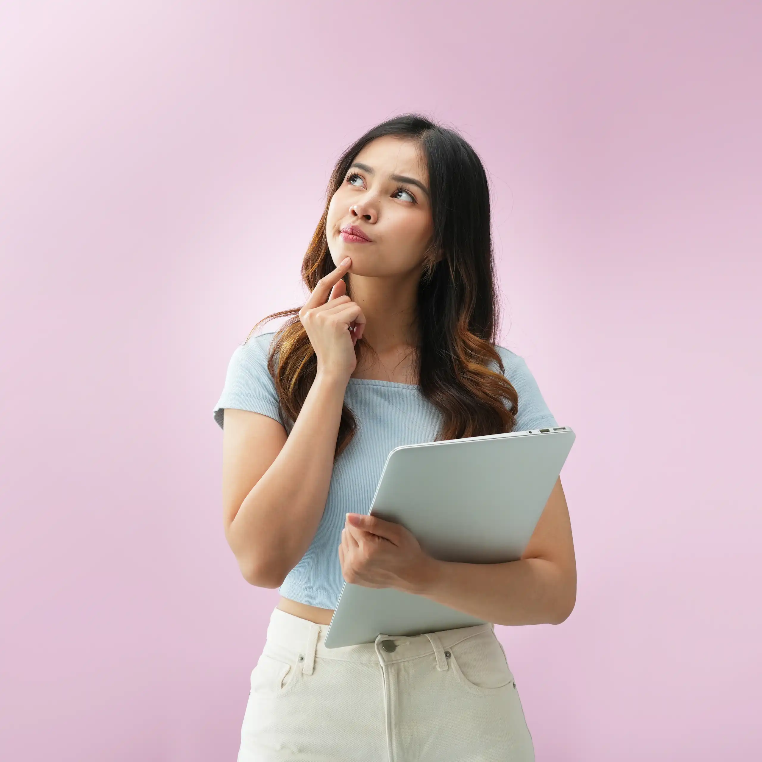 woman standing with laptop, looks questioning, pink background