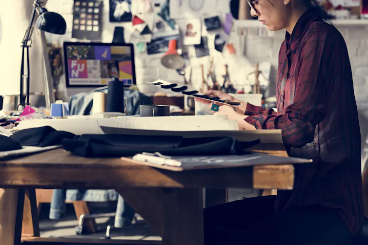 fashion designer sat at cluttered desk with samples of fabric