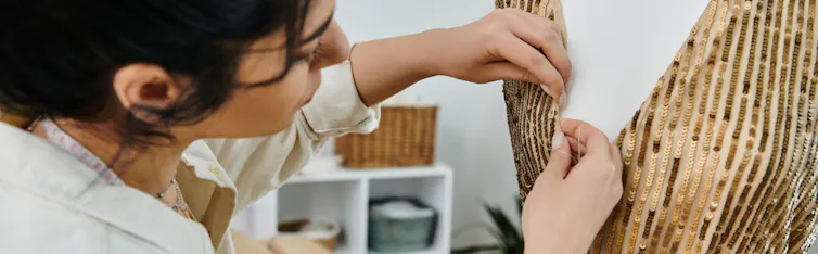 woman with dark hair, pins fabric to mannekin
